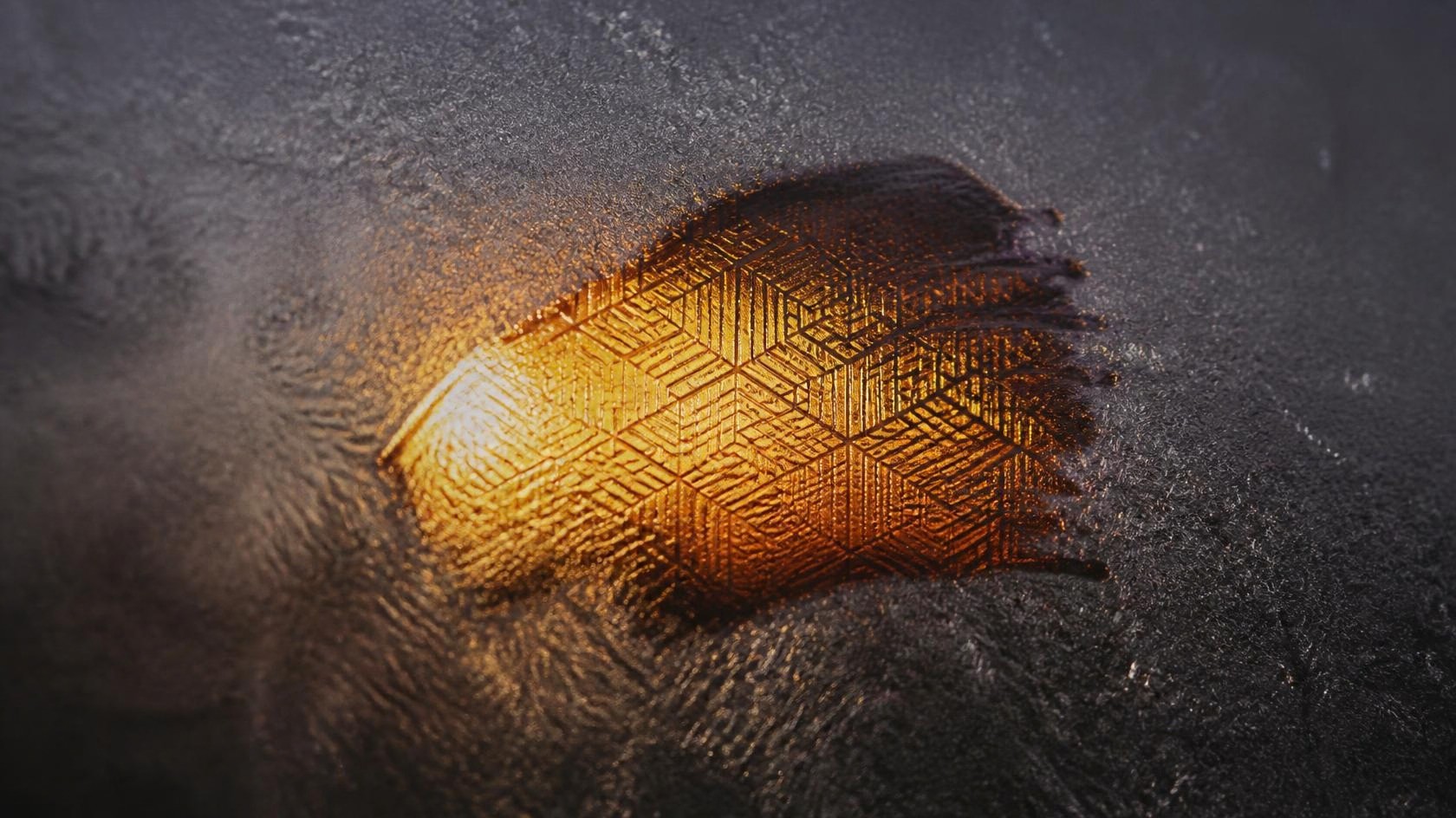A patch wiped through frost on dark glass, revealing a glowing amber pattern behind it