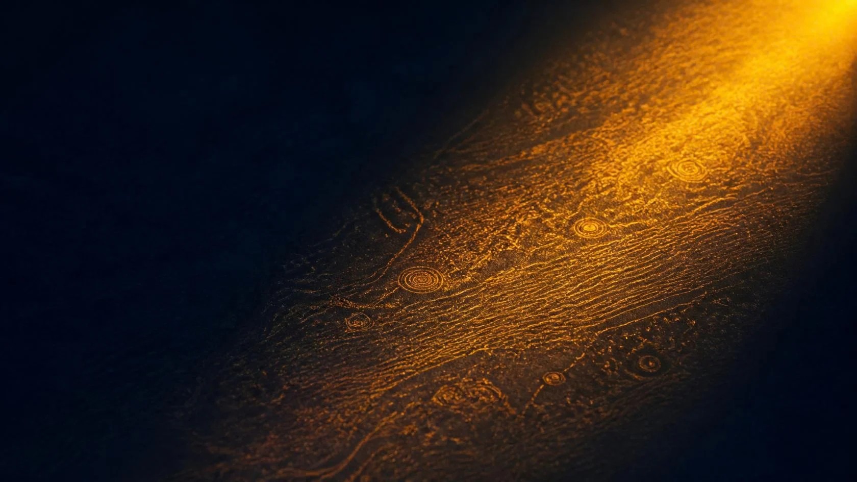 A dark surface with hidden marks showing only where a beam of amber light falls across it