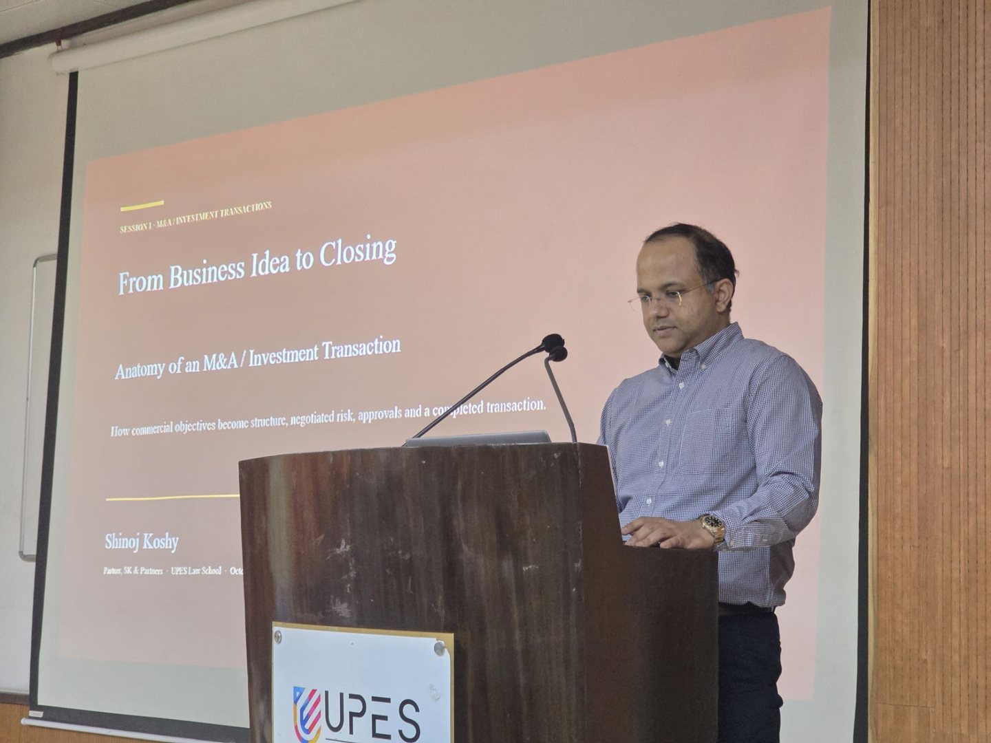 Shinoj Koshy at a lectern delivering a session titled From Business Idea to Closing: Anatomy of an M&A / Investment Transaction